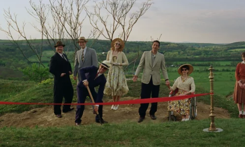 Une image du film 'The Brutalist' montrant un groupe de personnes en tenues d'époque sur une colline pour une cérémonie d'inauguration, avec un homme creusant le sol devant un ruban rouge.