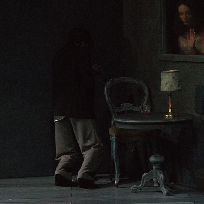 Un danseuse habillée en femme de ménage est adossé à un mur, on dirait se soutient la tête comme si elle s'était fait mal. Par une fenêtre, on aperçoit le buste d'une danseuse, l'encadrement de la fenêtre fait penser à un tableau figé.