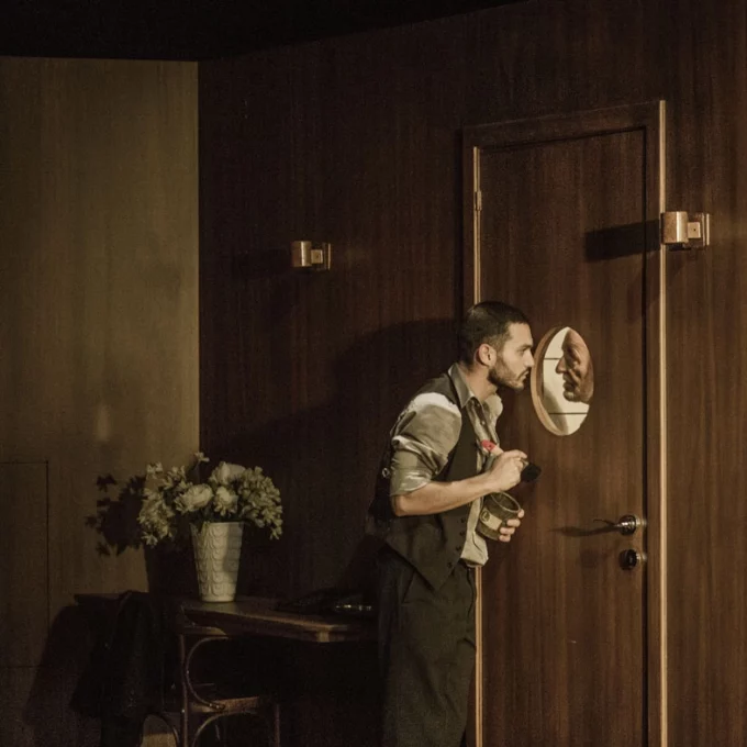 Deux danseurs se regardent à travers le hublot d'un porte. Le décors fait pensé à l'intérieur d'un bateau.