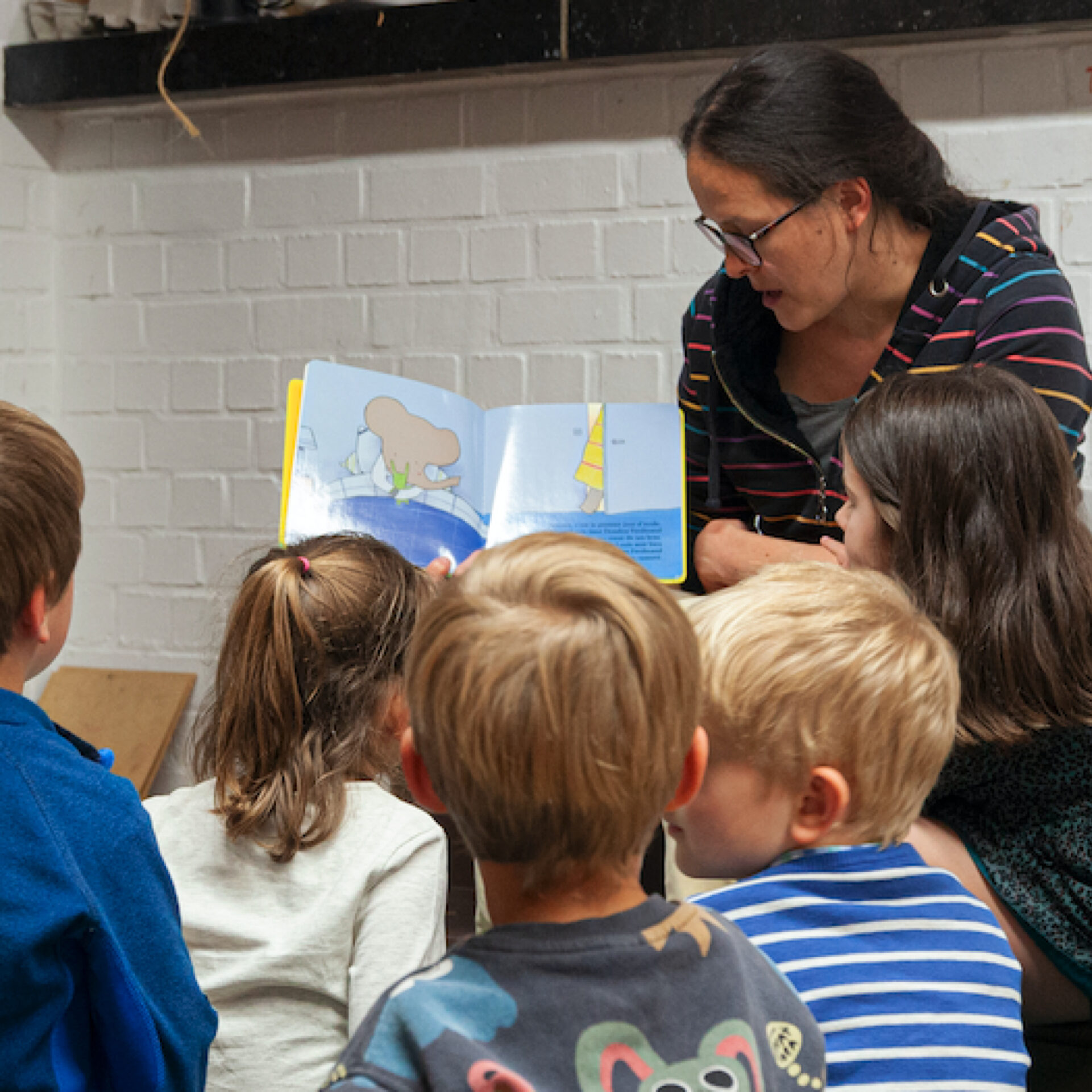 La conteuse tenant un livre qu'elle montre à quatre enfants.