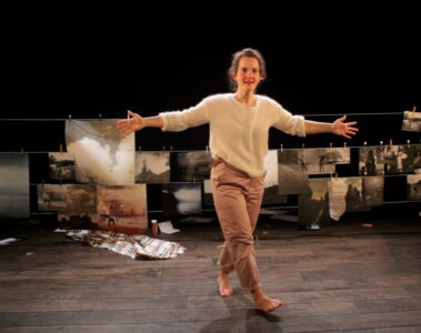 Kelly Rivière seule scène, debout les bras écartés avec en arrière plan des impressions photos accrochés à des pinces à linges. Elles semblent représenter des images de manifestations en Irlande.